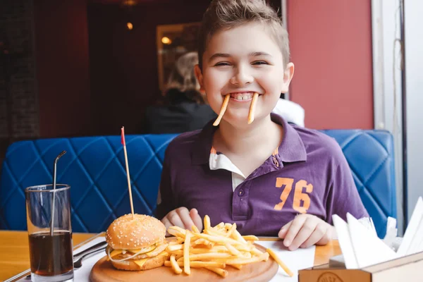 Engraçado menino comendo um hambúrguer em um café, conceito de comida — Fotografia de Stock