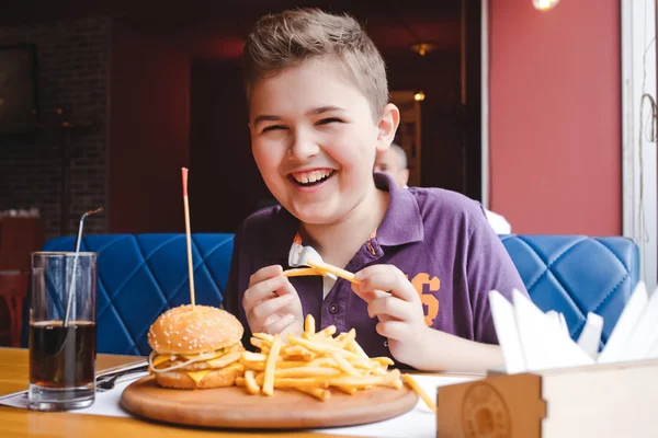 Забавный маленький мальчик ест гамбургер в кафе — стоковое фото