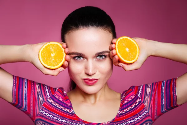 Portrait of comic happy girl holding halves of orange near face,