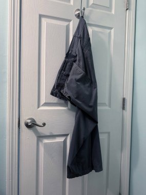 Banyoda kancaya asılı siyah pantolon.