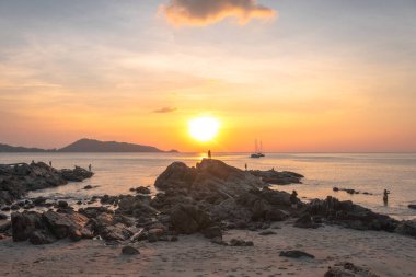 Dağın arkasındaki altın gökyüzü, baba ve oğul Kalim Sahili 'nde gün batımını izlemek için bir kayanın üzerinde duruyorlar.,