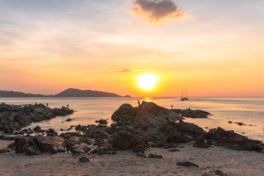 Dağın arkasındaki altın gökyüzü, baba ve oğul Kalim Sahili 'nde gün batımını izlemek için bir kayanın üzerinde duruyorlar.,