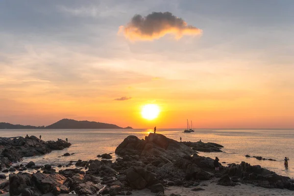 Golden sky behind the mountain, father and son stand atop a rock to watch the sunset at Kalim Beach,