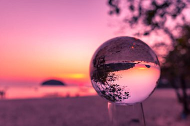 Kristal küre içinde Koh Pu ve Kata plajı arasında gün batımı görüntüsü, kristal kürede baş aşağı görünüyor.