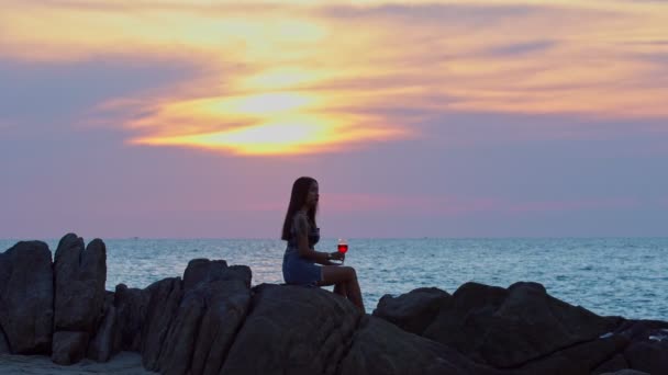 日落时带着酒杯在海滩上畅饮的年轻漂亮女子 — 图库视频影像