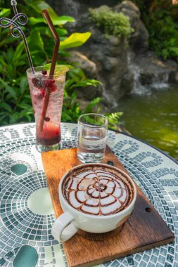 Seramik masaya konmuş bir dizi sıcak kahve içeceği. Bir şelalenin arka planı, yemyeşil, ve buhar onu taze göstermek için yüzüyordu.