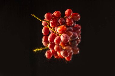 Aynaya yerleştirilmiş bir demet üzüm ve siyah bir arka plan.