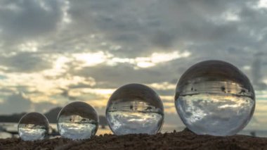 Kristal küreler halinde dizilmiş dört dünya gibi. Plaja yerleştirilmiş bir kristal küre günbatımındaki deniz manzarasının ters yansımasını görebilir. Eşsiz bir fikir için 4K videosu..