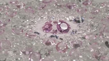 Pembe safir elmaslar farklı boyutlarda ve birçok şekil ortadaki beyaz zeminde kesilmemiş kırmızı taşlarla çevrili. 