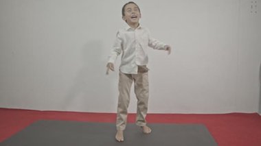 Beyaz arka planda kırmızı halıda çılgınca dans eden tatlı bir çocuk. Aktif eğlence ve yaşam tarzı konsepti. Stüdyo çekimi.