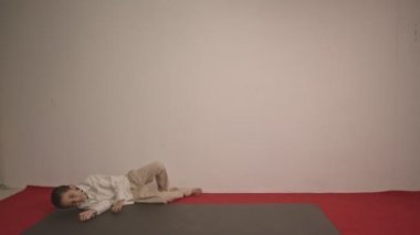 Beyaz arka planda kırmızı halıda çılgınca dans eden tatlı bir çocuk. Aktif eğlence ve yaşam tarzı konsepti. Stüdyo çekimi.