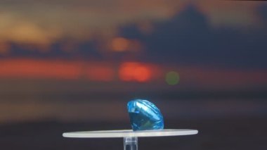  Aquamarine mavi elması vitrine yerleştirip dönmeye devam et. Video 4k... deniz arka planında 4K günbatımı yüksek kaliteli video.