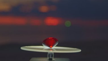 Kırmızı elmas vitrine yerleştirilmiş ve dönmeye devam ediyor. Video 4k... deniz arka planında 4K günbatımı yüksek kaliteli video.