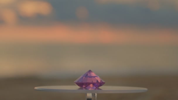 回転ショーケースに置かれたピンクのダイヤモンドを回し続けます ビデオ4K 海の背景に高品質のビデオ4Kサンセット — ストック動画