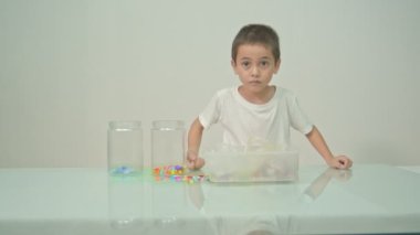 Sevimli bir çocuk beyaz odadaki çok renkli boncukları seve seve çaldı. Yüksek kalite video 4K. Stüdyo çekimi.