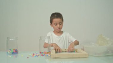 Sevimli bir çocuk beyaz odadaki çok renkli boncukları seve seve çaldı. Yüksek kalite video 4K. Stüdyo çekimi.