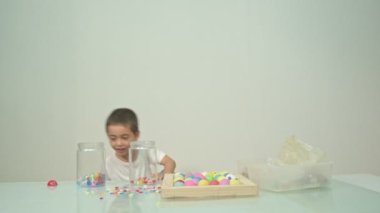 Çocuk beyaz odadaki cam bir kavanozda çok renkli boncukları salladı. Yüksek kalite video 4K. Stüdyo çekimi.