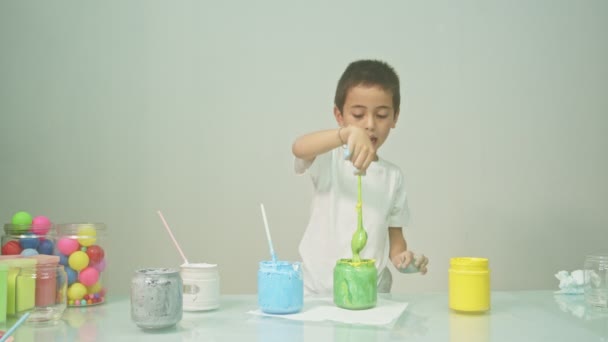 一个男孩子高兴地混合着一种新的颜色 男孩子在学校里混合着各种颜色的学习材料 蒙台梭利方法由孩子们管理 彩色背景 — 图库视频影像