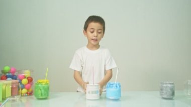Bir çocuk sevinçle yeni bir rengi karıştırıyordu. Çocuk okulda renkleri karıştırıyordu, çocukların yönettiği Montessori metodu. Yüksek kaliteli 4K video stüdyosu. renkli arkaplan.