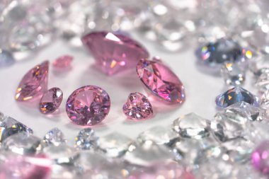 Beyaz arka planda, beyaz elmasların arasına yerleştirilmiş bir grup pembe elmas.