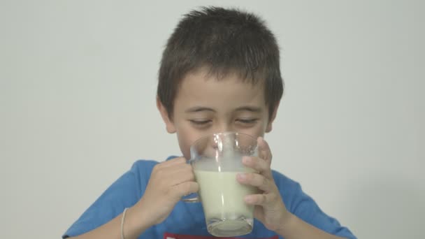 青いシャツを着たかわいい少年は 牛乳の味を知り 牛乳の味を説明しました そして顔を通して感情を示します スタジオの肖像画 白い背景を持つ概念の健康 — ストック動画