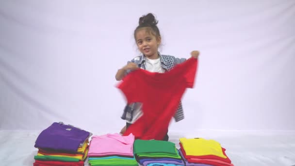 Мальчик Клетчатой Рубашке Держащий Красную Рубашку Раскачивающуюся Куче Разноцветных Рубашек — стоковое видео