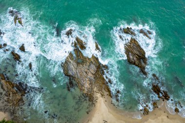 Yeşil denizdeki beyaz dalgaların havadan görünüşü yaz günü büyük kayalara çarpar..