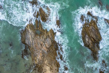 Yeşil denizdeki beyaz dalgaların havadan görünüşü yaz günü büyük kayalara çarpar..