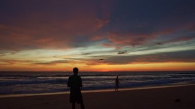 Günbatımında sarı gökyüzünde çarpıcı renkli bulutlar. Gün batımında çarpıcı, sarı gökyüzünde İHA uçuran bir adam. Güzel günbatımının fotoğraflarını çekmek için İHA kullanan turistler