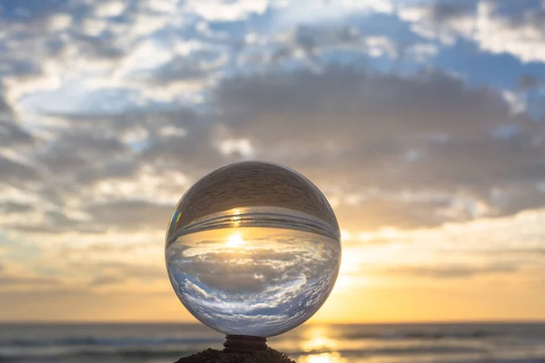 ビーチの横の木の上に置かれたクリスタルボールの中の美しい雲と黄金の夕日 — ストック写真