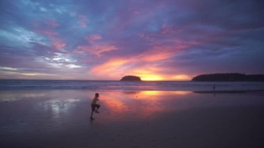 Gün batımında plajda koşan mutlu bir çocuk. 4K UHD. Mavi gökyüzü ve renkli bulutları olan güzel tropikal bir plaj. Dalgaların boş plajı vurduğu tropik sahil. Phuket Tayland 'da..