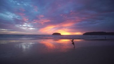 Gün batımında plajda koşan mutlu bir çocuk. 4K UHD. Mavi gökyüzü ve renkli bulutları olan güzel tropikal bir plaj. Dalgaların boş plajı vurduğu tropik sahil. Phuket Tayland 'da..