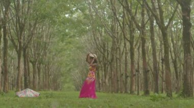 Güzel elbiseli bir kadın ağaç tünelinde yürüyor. Lastik plantasyondaki ağaç tüneli. Yeşil orman arka planı. 4K Yüksek kaliteli video.