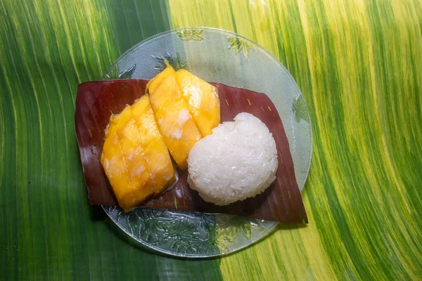 Mango sticky rice served on a spotted banana leaf by the pool.speckled banana leaves in the background.beautiful green and yellow color of nature background. food and restaurant concept.