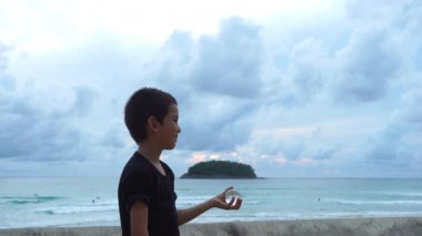 Bir çocuk elinde kristal bir topla kumsalda oturuyor.