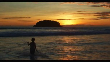 Altın gün batımında plajda oynayan bir çocuk. Cennet sahili mavi denizi ve temiz kumsal manzarası. komik çocuk ve seyahat konsepti.