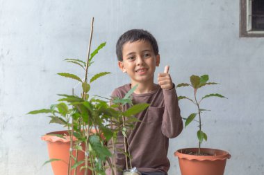 Mutlu bir çocuk Kratom ağaç fideleriyle eğlenir. Sevimli bir çocuk mutlu bir gülümsemeyle bir ağaca sarıldı. Mutlu gülen surat, ağaçları seviyorum. Mutlu çocuğun gülümseyen yüzü rahatla dünya konseptini kurtar.