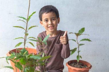 Mutlu bir çocuk Kratom ağaç fideleriyle eğlenir. Sevimli bir çocuk mutlu bir gülümsemeyle bir ağaca sarıldı. Mutlu gülen surat, ağaçları seviyorum. Mutlu çocuğun gülümseyen yüzü rahatla dünya konseptini kurtar.
