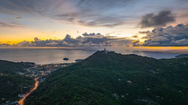 Nefes kesen bir gün batımının hava hiper yanılma görüntüsü sahneyi çevreleyen yemyeşil tepelerle dolu kıyı kasabasının üzerinde turuncu ve mavi renkli gökyüzünü resmediyor. Okyanusun üzerinde dramatik gün batımı bulutu