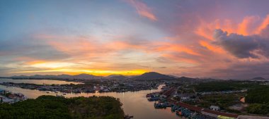 Phuket 'teki balıkçı limanında sersemletici gün batımını gösteren hava manzarası. Yumuşak mor renkten ateşli turuncu renklere dönüşen canlı gökyüzü, sakin ve pitoresk bir atmosfer yaratır..  