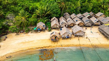 Phang Nga, Tayland-Mart, 20.2025: Yeşillik yeşil ormanlarla çevrili kıyı şeridi boyunca sıralanmış küçük kulübeleriyle tropikal bir sahil Morgan köyünün çarpıcı hava manzarası. Balıkçı tekneleri demirli.