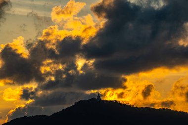 The majestic Big Buddha overlooks the island as the sun sinks behind the horizon. The mountain glows softly in shades of amber, capturing the harmony between nature, light, and spirit.