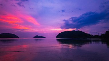 Surin Adaları üzerinde çarpıcı bir günbatımının havadan görüntüsü. Sakin okyanus sularına yansıyan altın renklerle. Sahil şeridindeki mercan resifi derinlik katıyor. Şnorkel için cennet