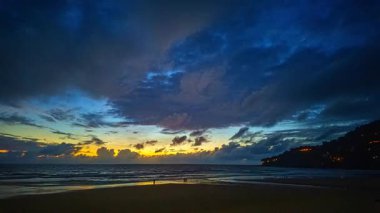 Havanın turuncu ve mavi tonlarında parladığı kumlu plajın tadını çıkaran insanlarla okyanusun üzerinde çarpıcı bir günbatımı. Sıcak ışık ve sakin dalgalar huzurlu ve resimli bir sahil manzarası yaratır..