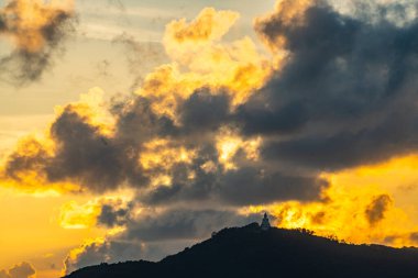 Zaman atlaması alacakaranlığın altın sıcaklığında yıkandı, Phuket Büyük Buda dağın zirvesinde sessiz bir zarafet içinde duruyor, canlı bulutlar ve dingin bir gökyüzü tarafından çerçevelenmiş gerçek bir ruhani merak anı..
