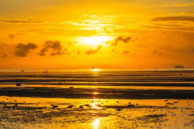 A breathtaking view of the sun setting over the ocean. casting a golden glow across the sky and reflecting on the water. A lone structure stands in the distance. adding depth to the serene coastal scene.  