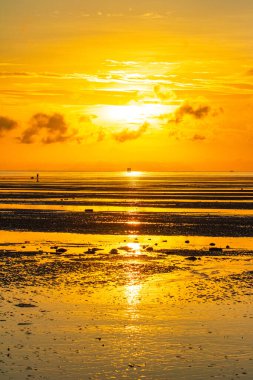 A breathtaking view of the sun setting over the ocean. casting a golden glow across the sky and reflecting on the water. A lone structure stands in the distance. adding depth to the serene coastal scene.  