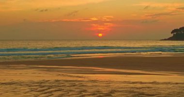 Gün batımının yansımalarının hava görüntüsü ıslak kumda dans ediyor, gökyüzünün rengarenk parıltısını yansıtıyor. Dalgaların hafif kükremesi fısıldayan rüzgarla uyumlu hale gelir. Güzel Karon plajı gün batımında.