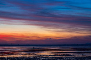 Pembe ve turuncu renkli canlı bir günbatımının çarpıcı bir sahnesi Karon plajı Phuket 'in üzerinde gökyüzünü aydınlatıyor. Huzurlu su huzurlu ve atmosferik bir manzara yaratır.
