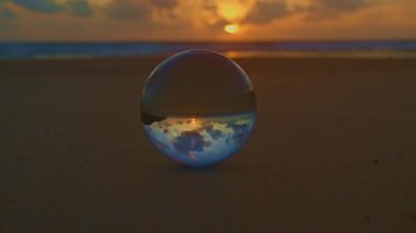 Cam küre sahilde gün batımını yansıtıyor.